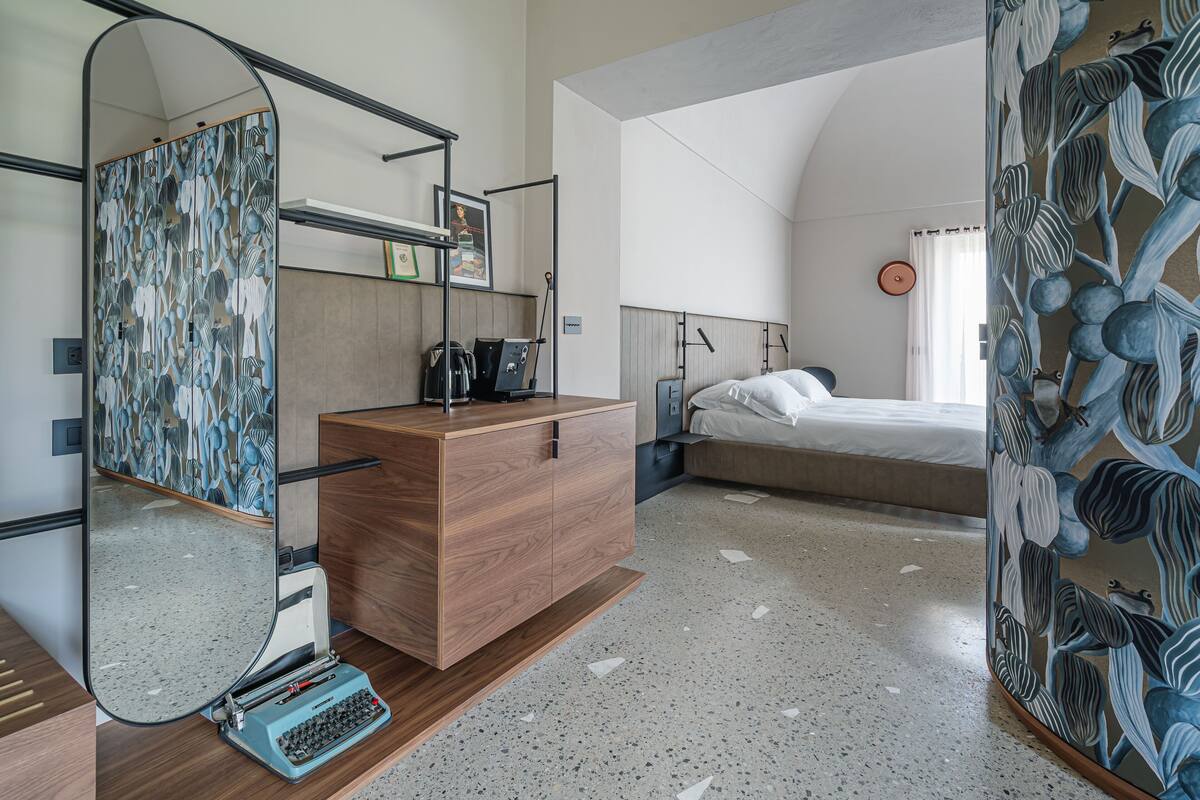 A modern hotel room with a wooden dresser, a mirror, a bed, and a wall with a floral pattern.