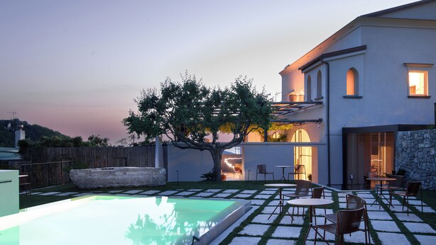 Una casa moderna con piscina, mobiliario exterior y un gran árbol.