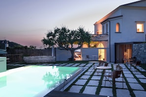 A modern house with a swimming pool, outdoor seating, and a large tree.
