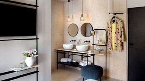 Un baño moderno con dos lavabos, un espejo, un televisor y un perchero para bata.