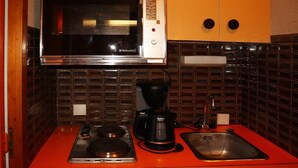 Een kleine keuken met een magnetron, koffiezetapparaat en een compacte koelkast.