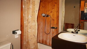 Een badkamer met een douchecabine van hout, een toilet, een wastafel met spiegel en een papieren handdoekdispenser.