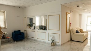 Un vestíbul ample amb terra de marbre, una armchair blava, un sofà beix i una taula de recepció amb mirall.