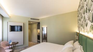 Une chambre d’hôtel avec un lit, un bureau et une chaise, une télévision et une salle de bain visible à travers une porte ouverte.