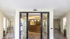 A modern hotel lobby with a marble floor, glass doors leading to a reception area, and pendant lighting. - Solmaris Tropea - Rooms & Suites (Tropea)