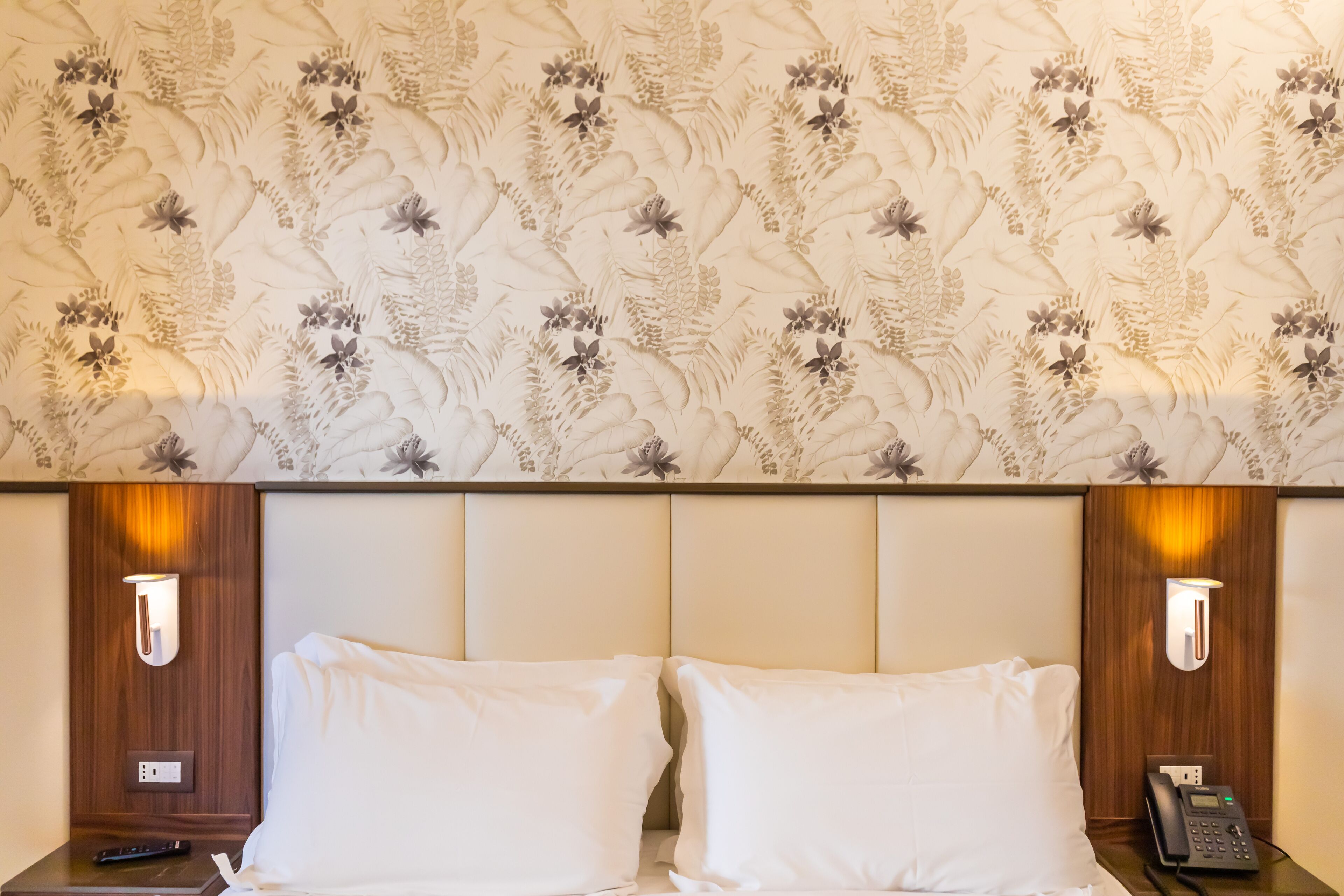 Une chambre d’hôtel avec un papier peint à motifs floraux, deux tables de chevet avec des lampes, un téléphone et une télécommande.