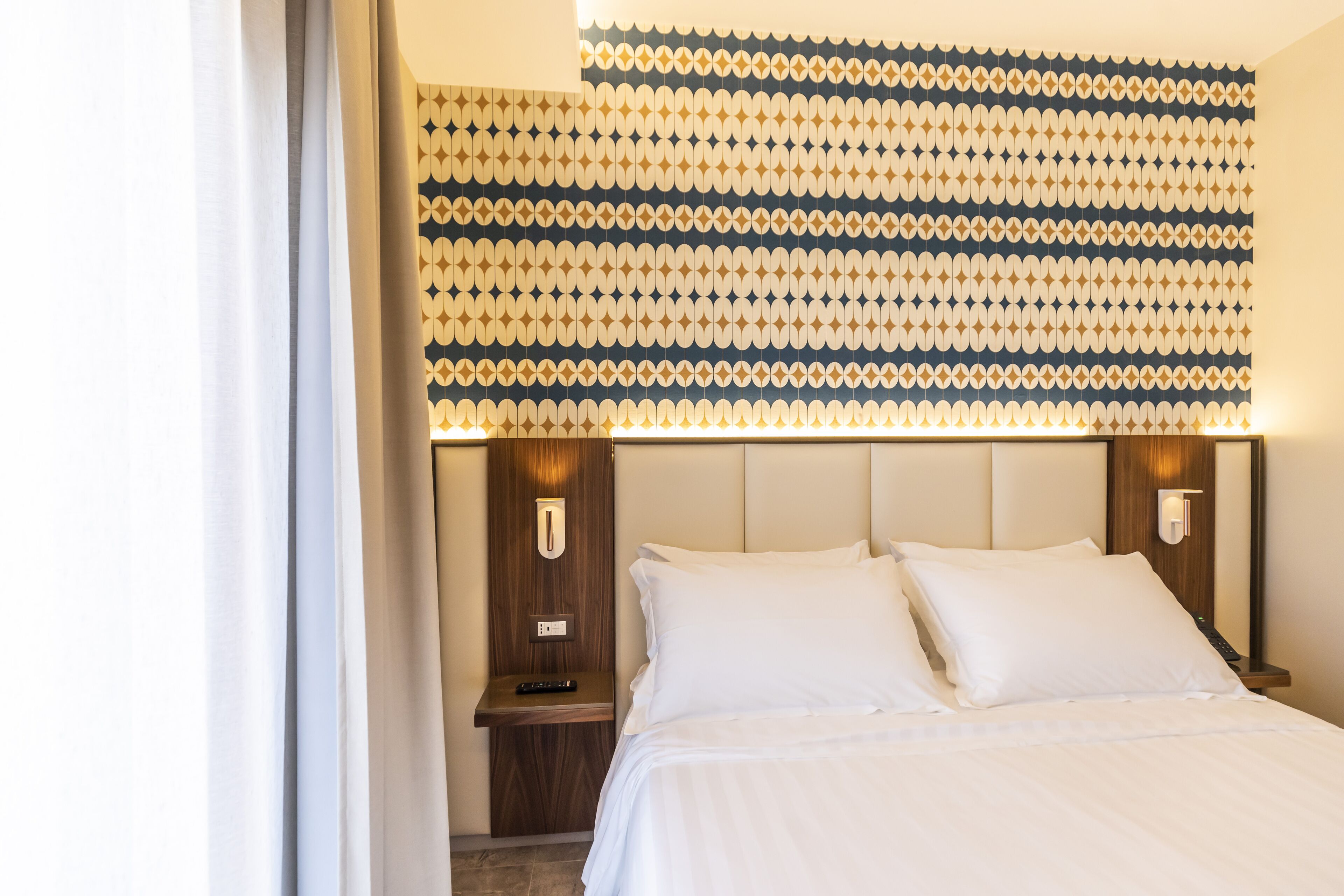 Une chambre d’hôtel avec un lit, des tables de chevet et un mur décoré d’un motif.