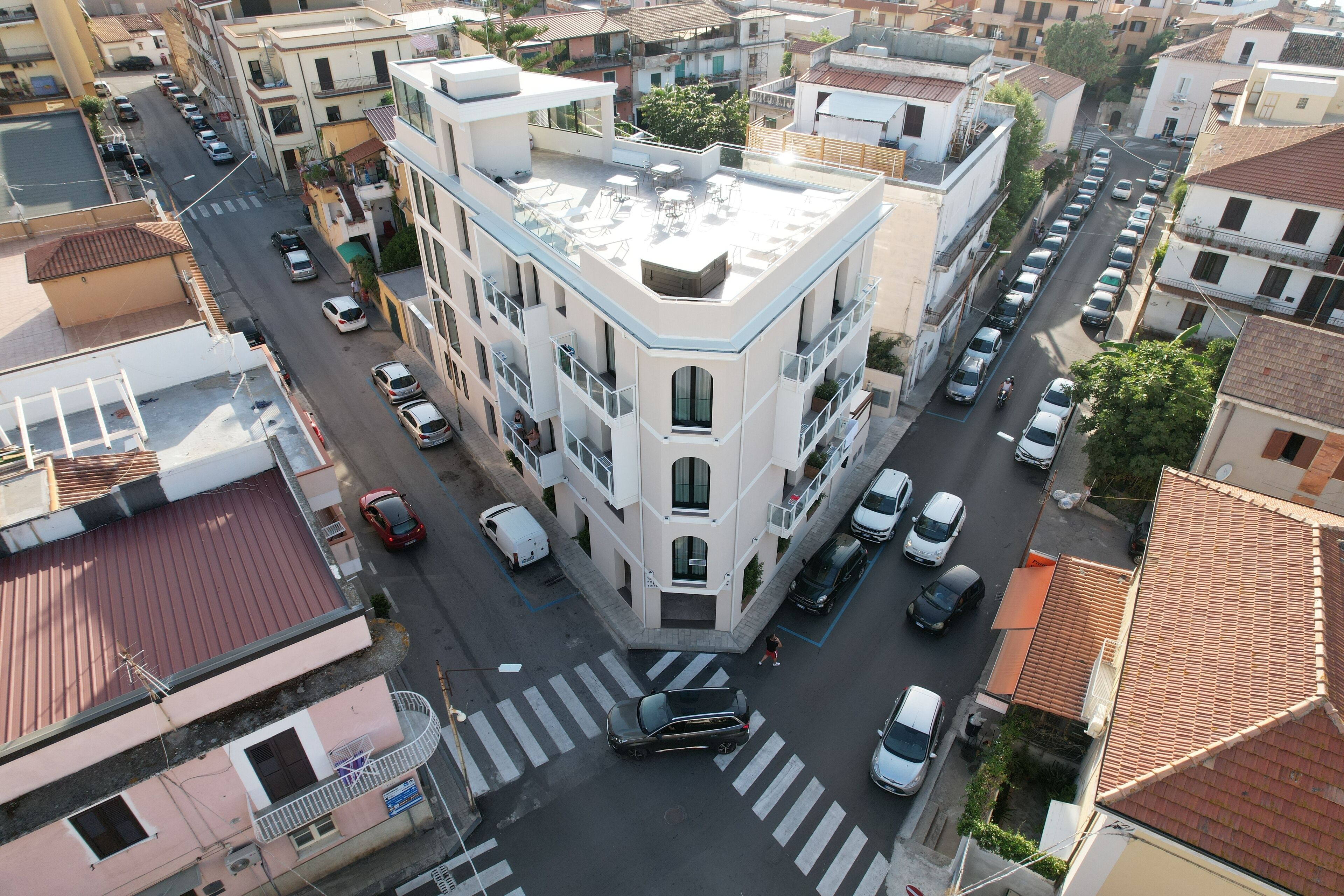 Un immeuble à plusieurs étages doté d’une terrasse sur le toit, d’un passage piéton et de voitures garées.