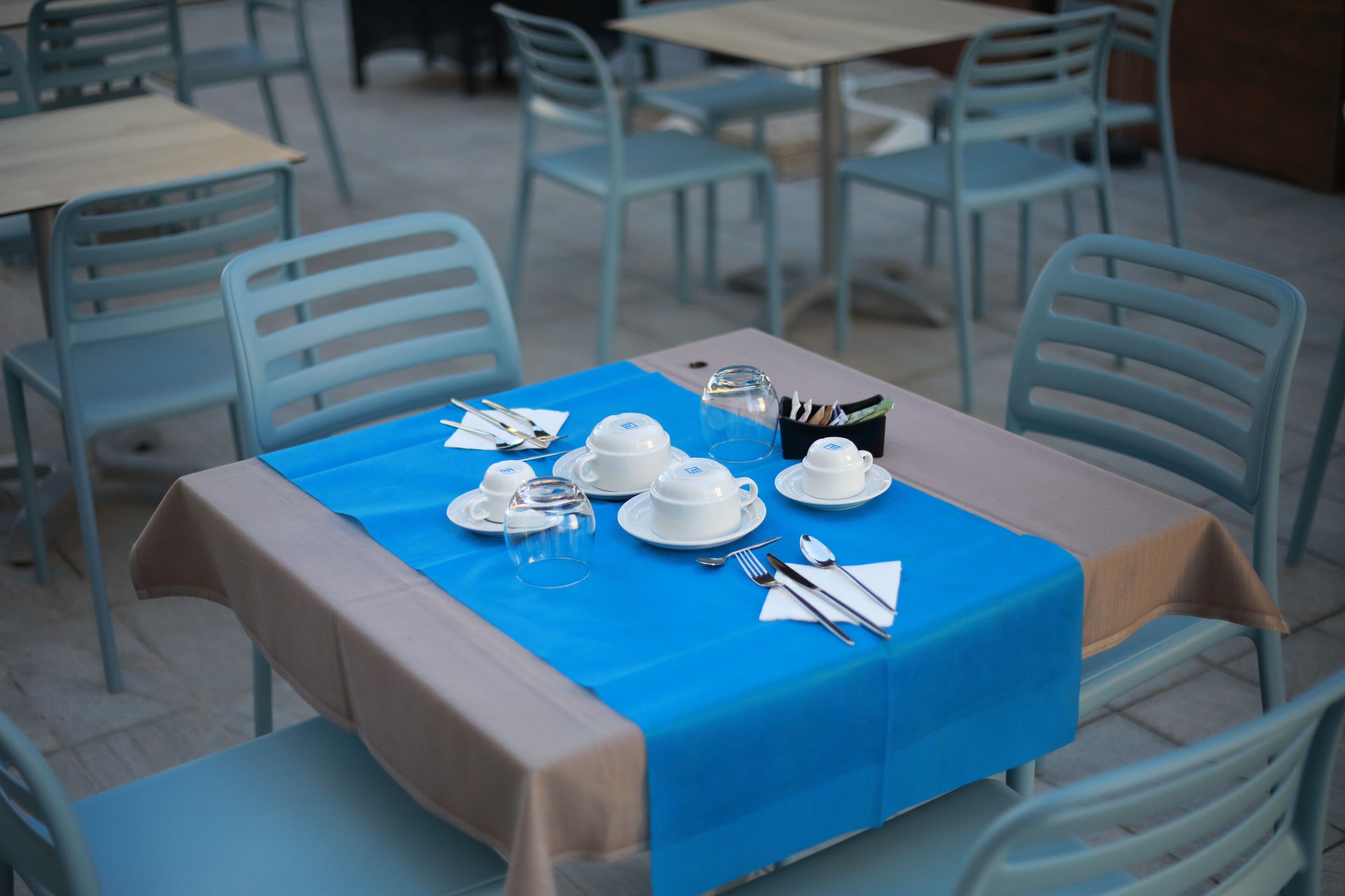 A table set for four with a blue tablecloth, white plates, cups, and cutlery.