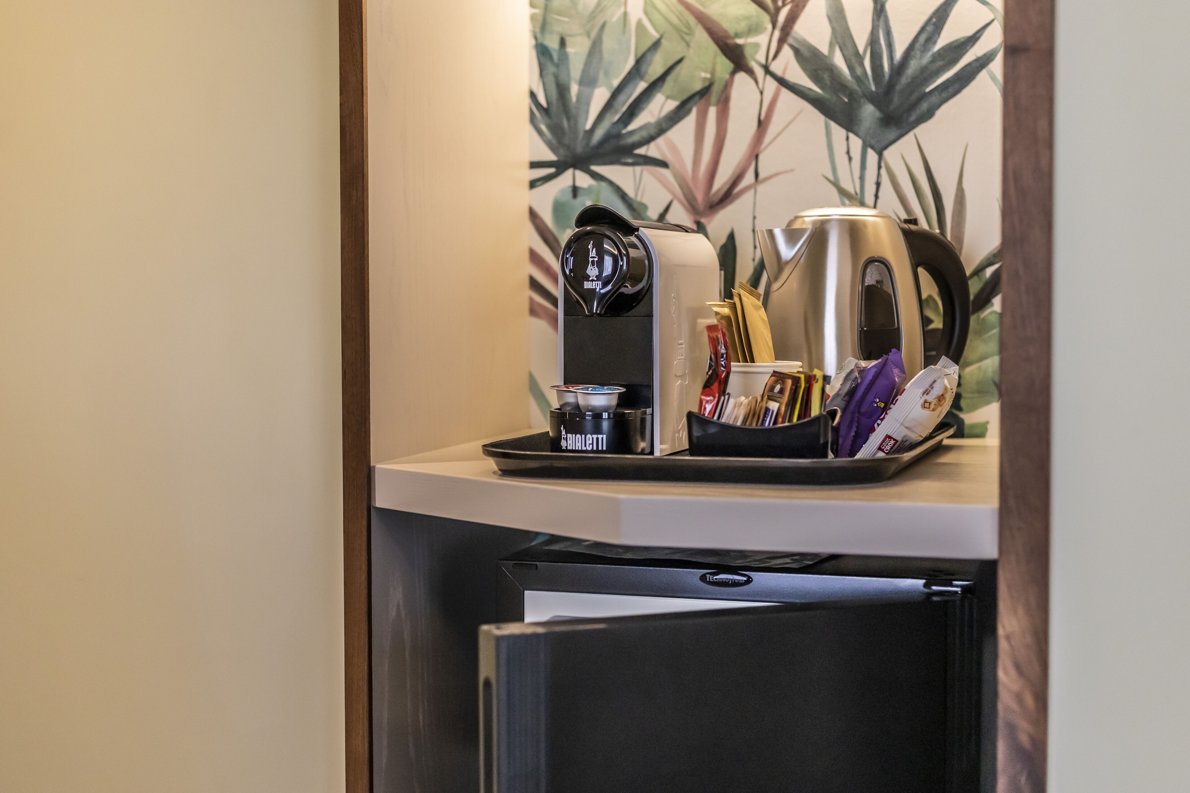 A compact kitchenette with a coffee maker, a kettle, and a tray with utensils and a cup.