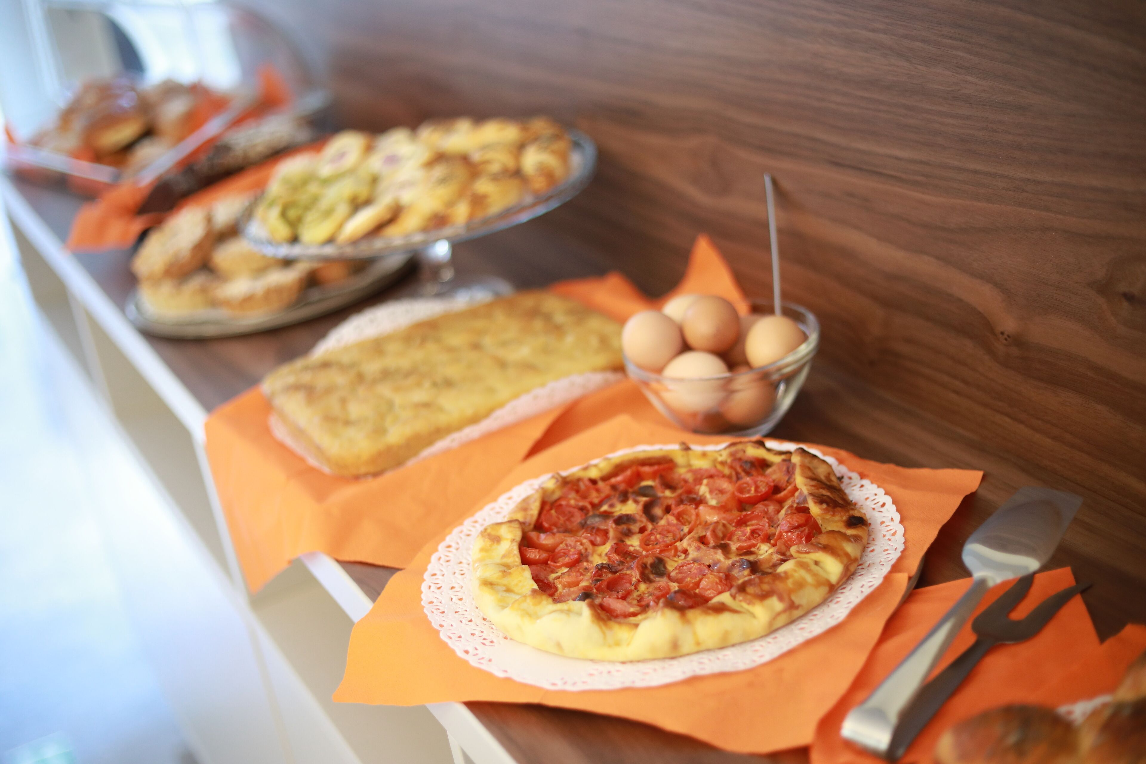 Variedad de productos horneados sobre una mesa de madera, incluyendo pizza, quiche y varias pastas.