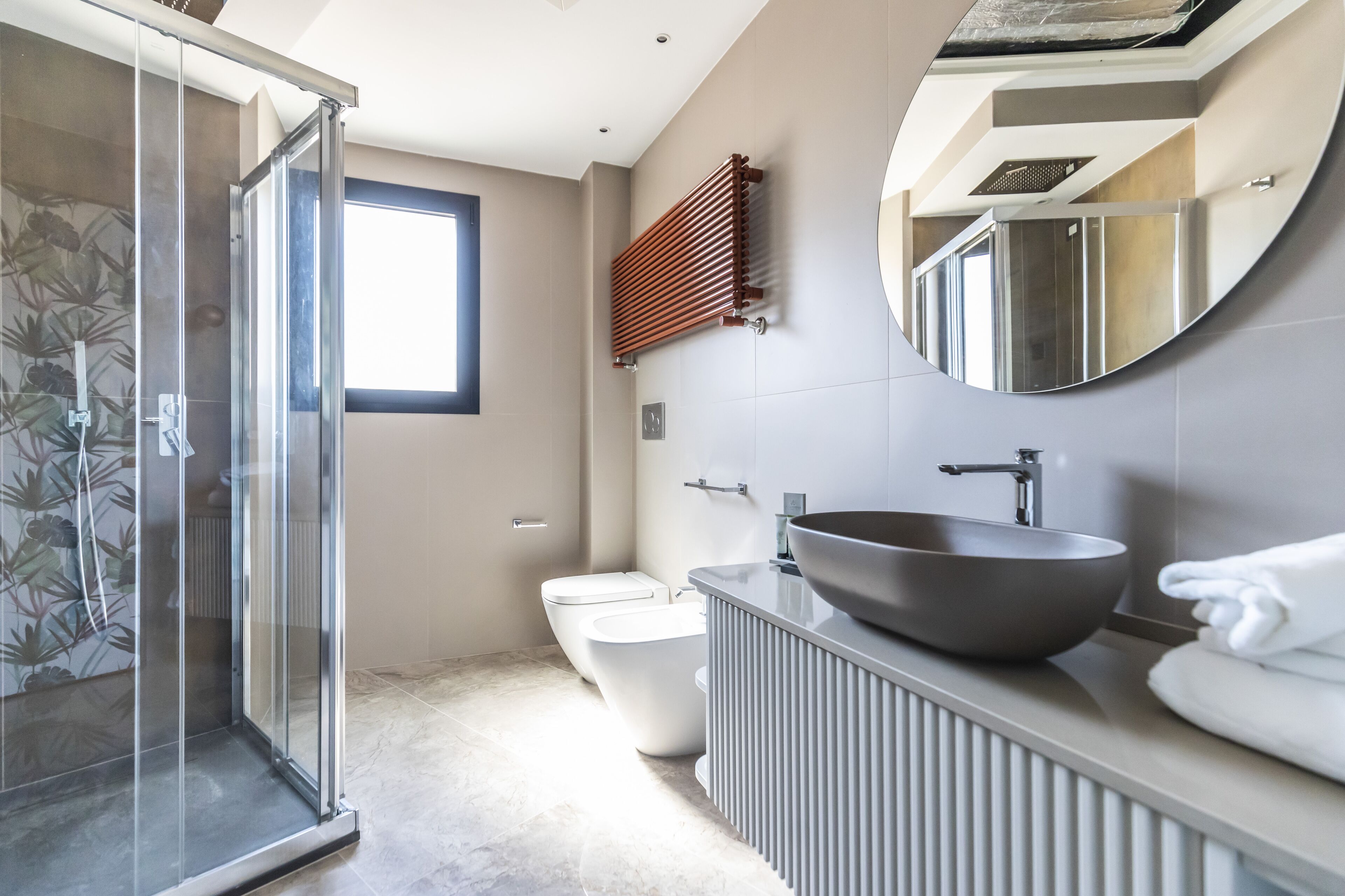 Un baño moderno con cabina de ducha de vidrio, inodoro blanco, bidé y un lavabo de diseño amplio.