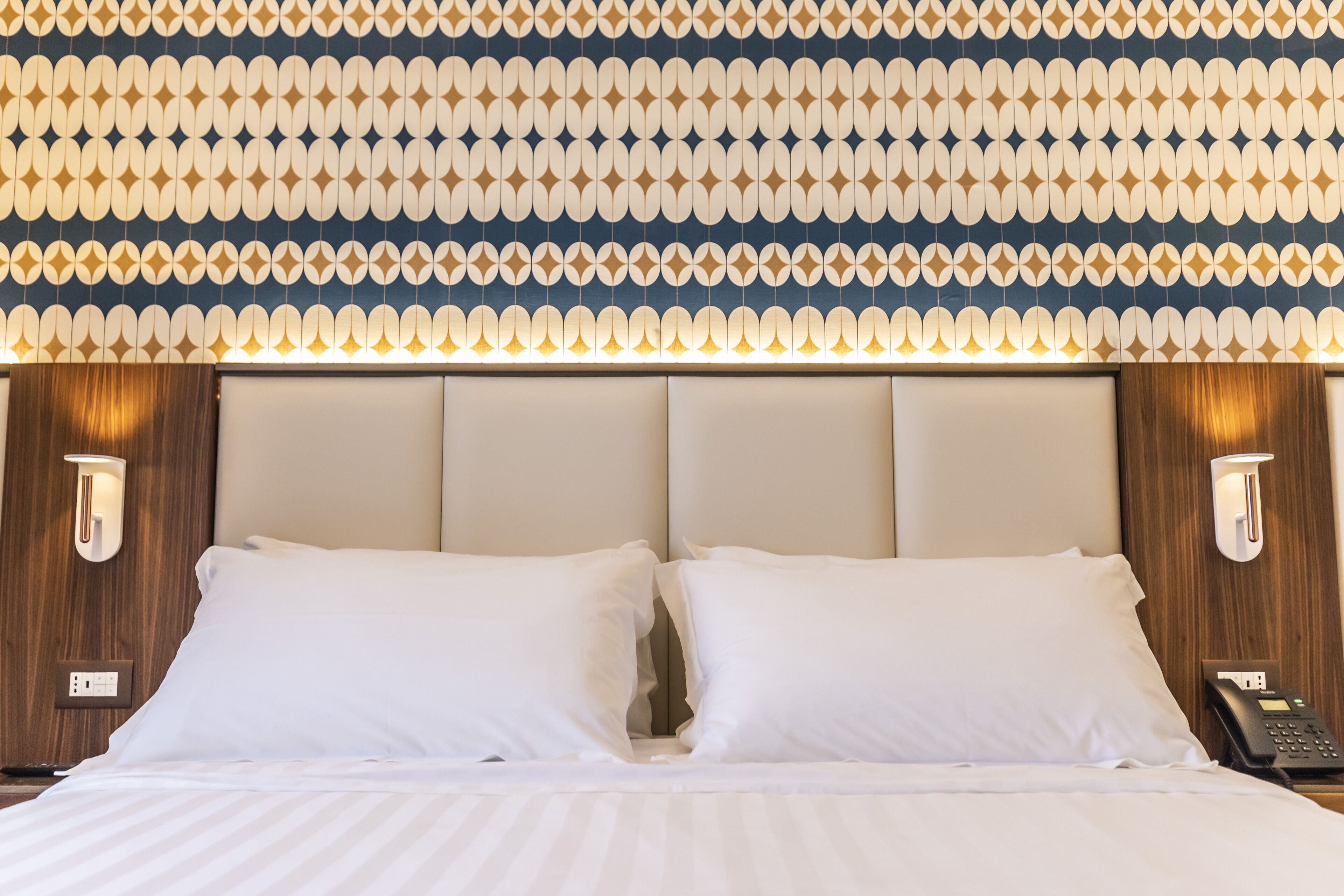 A hotel room with a large bed, two bedside lamps, and a patterned wall.