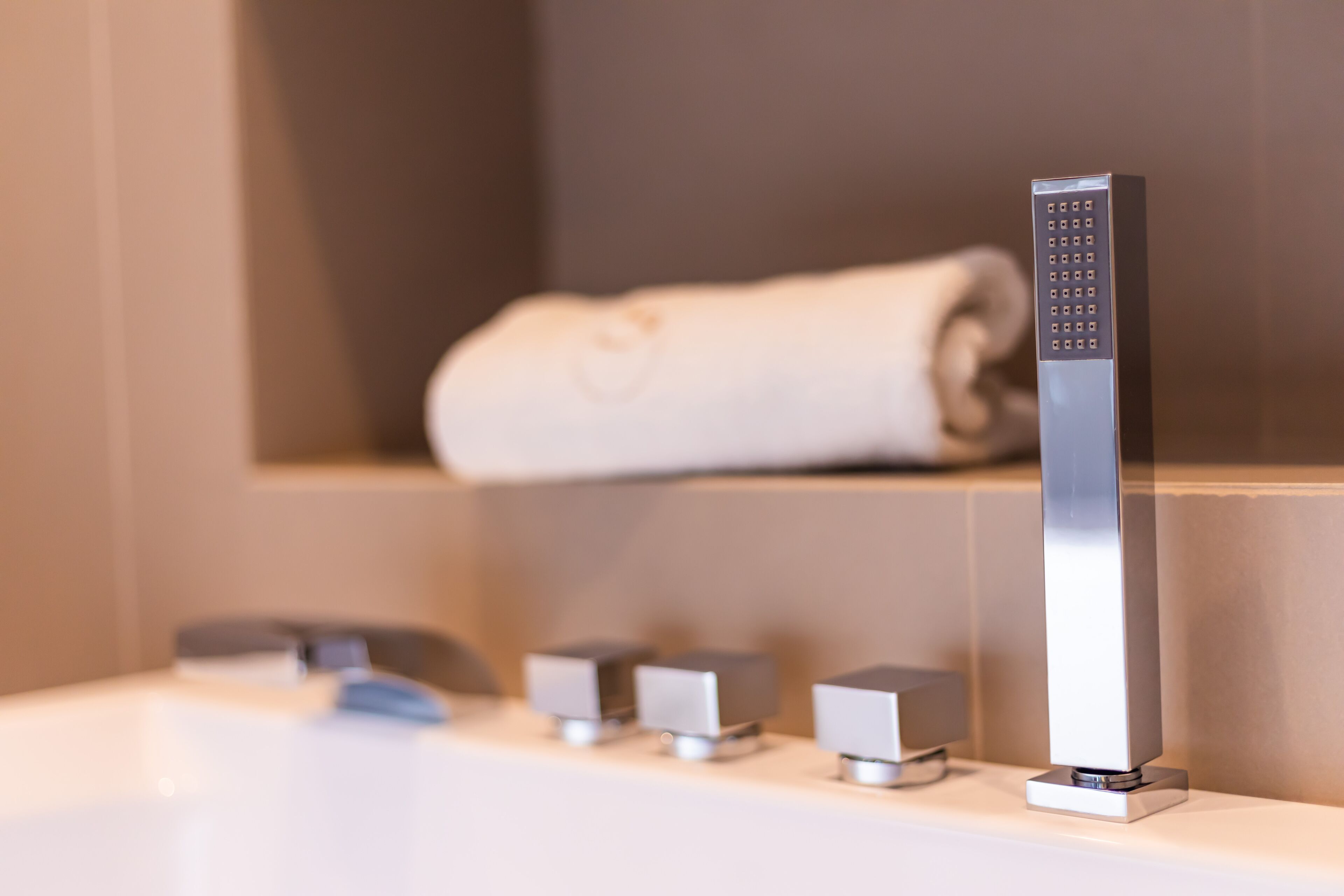 Une salle de bain moderne dotée d’un panneau de commande vertical pour la douche, d’un porte-serviettes et d’un lavabo avec plusieurs robinets.