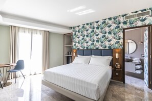 Habitación de hotel con una cama grande, un escritorio con silla, armario, baño con espejo y cabina de ducha.