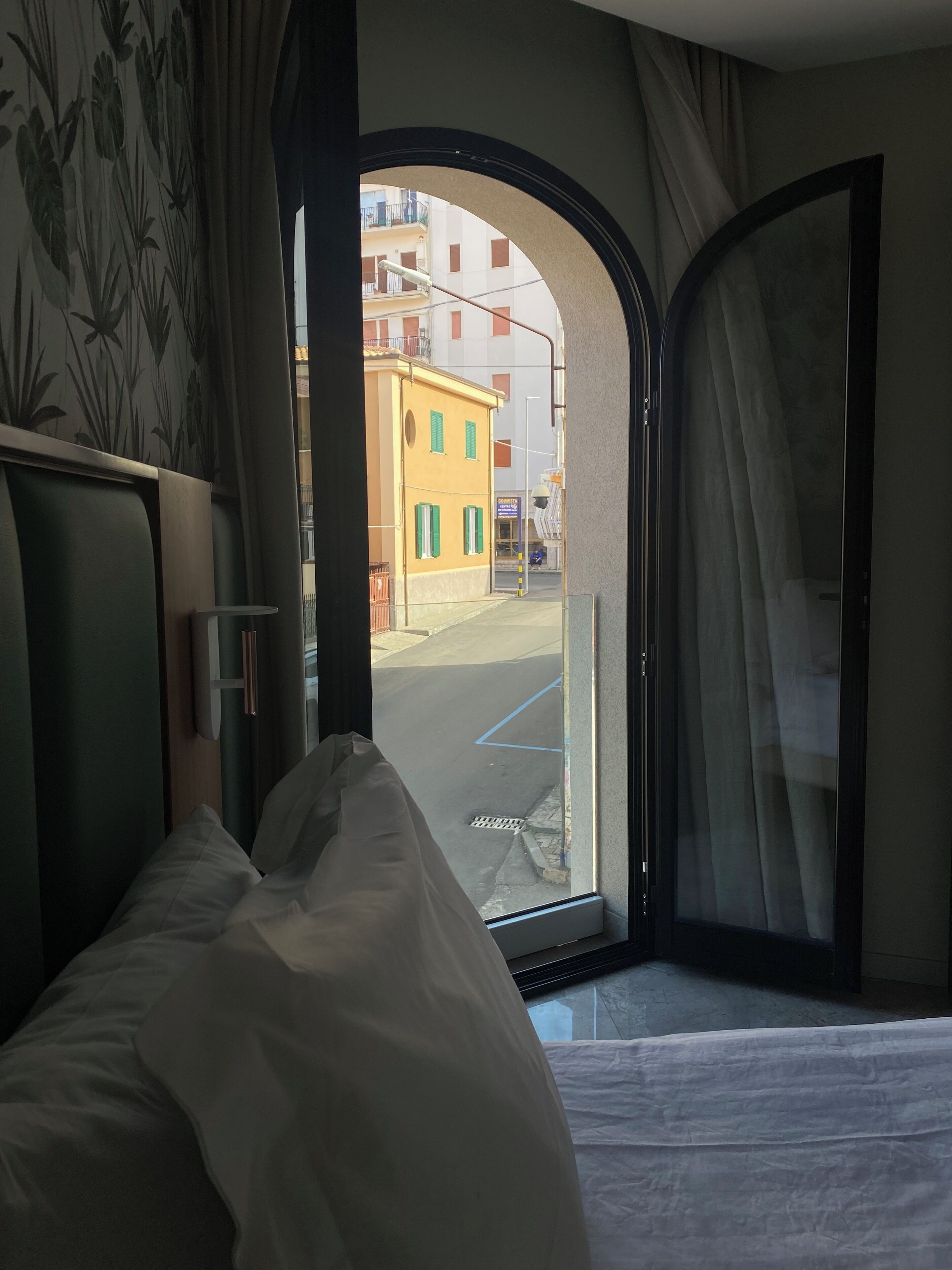 Una habitación de hotel con cama, ventana que da a la calle y edificios, y una cortina.