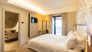 A hotel room with a large bed, a round mirror, a television, and a bathroom with a sink and toilet. - Solmaris Tropea - Rooms & Suites (Tropea)