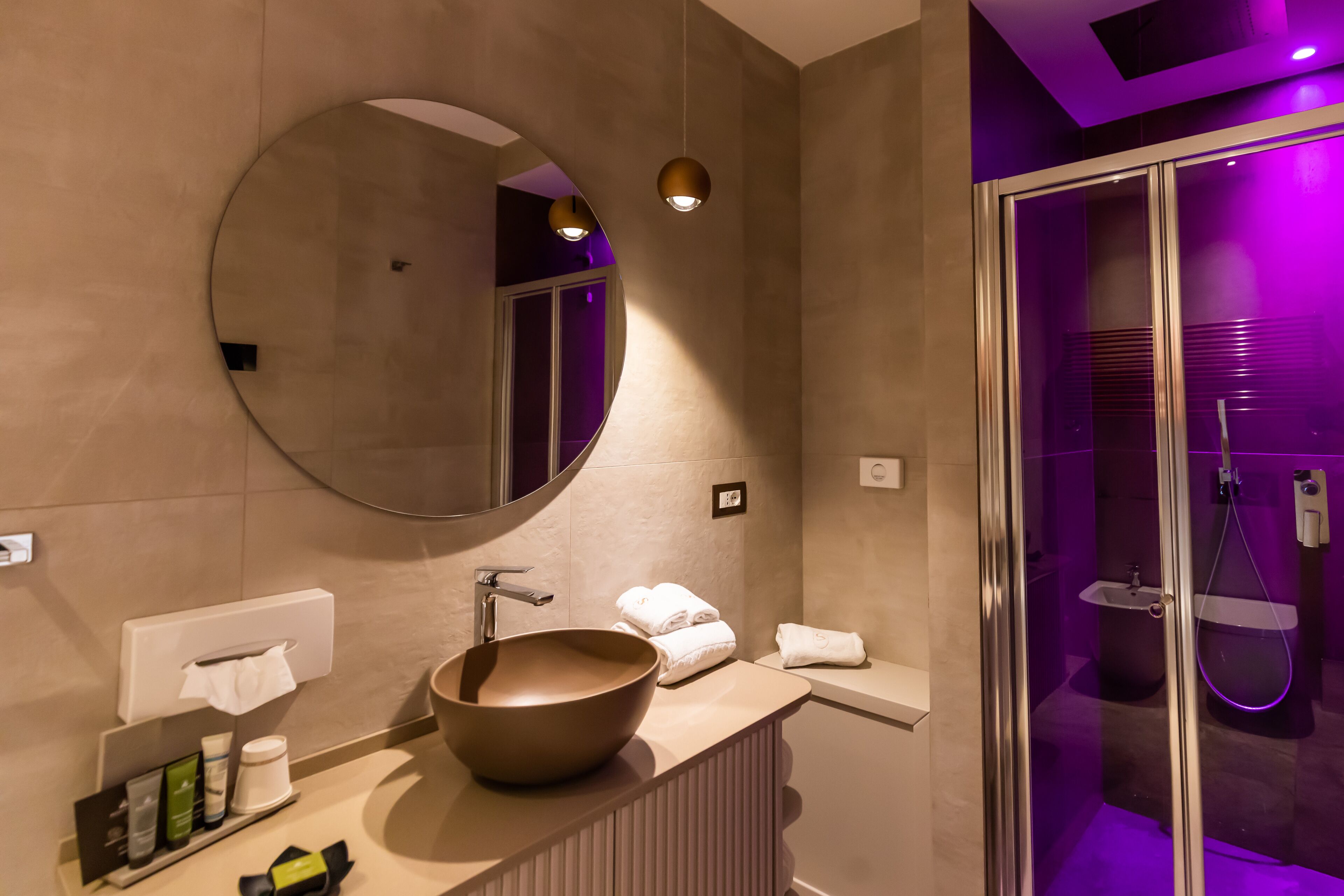 Un baño moderno con un espejo redondo grande, un lavabo sobre encimera y una ducha con mampara de cristal.