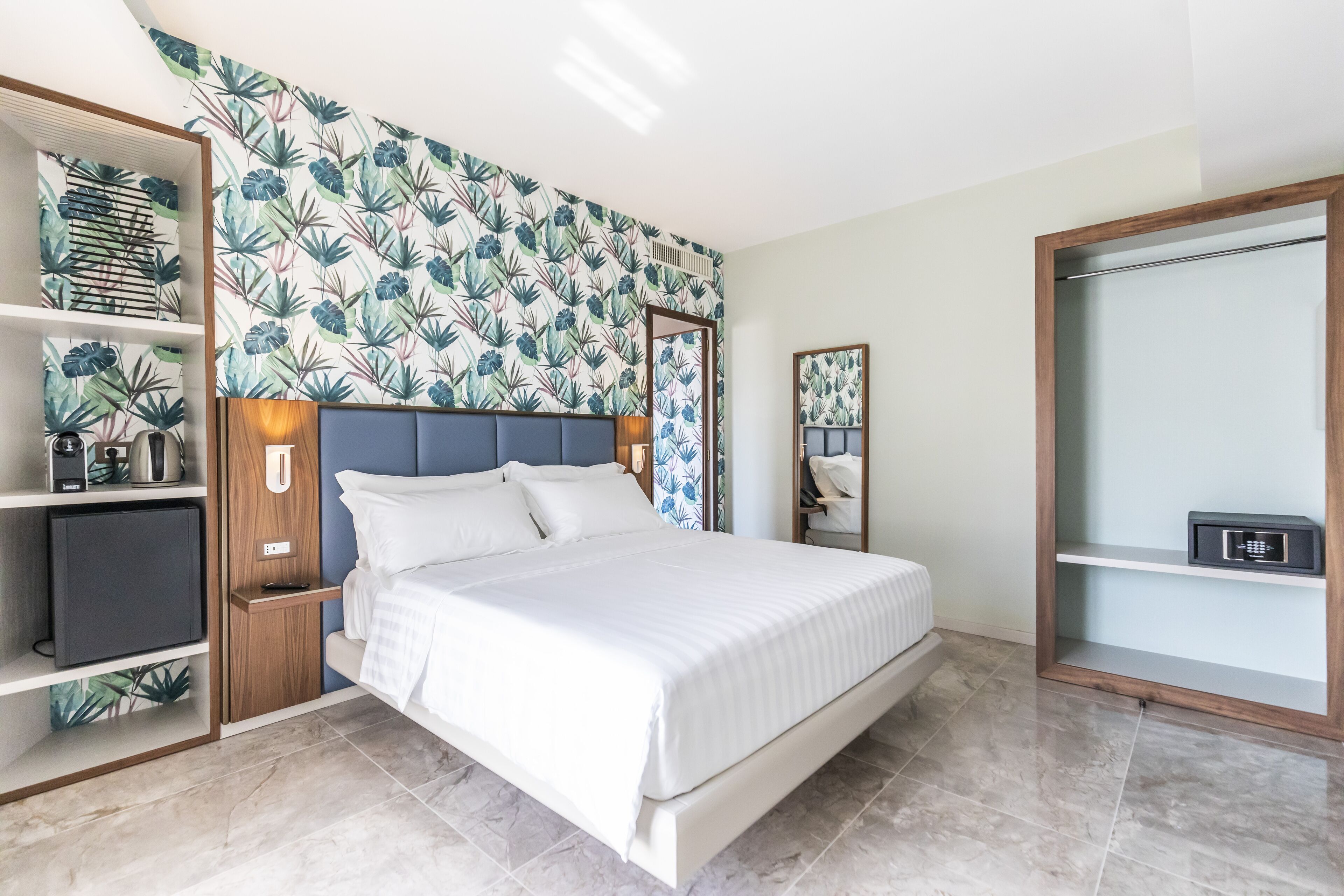 Un dormitorio moderno con cama, estanterías empotradas, armario y un papel tapiz con temática tropical.
