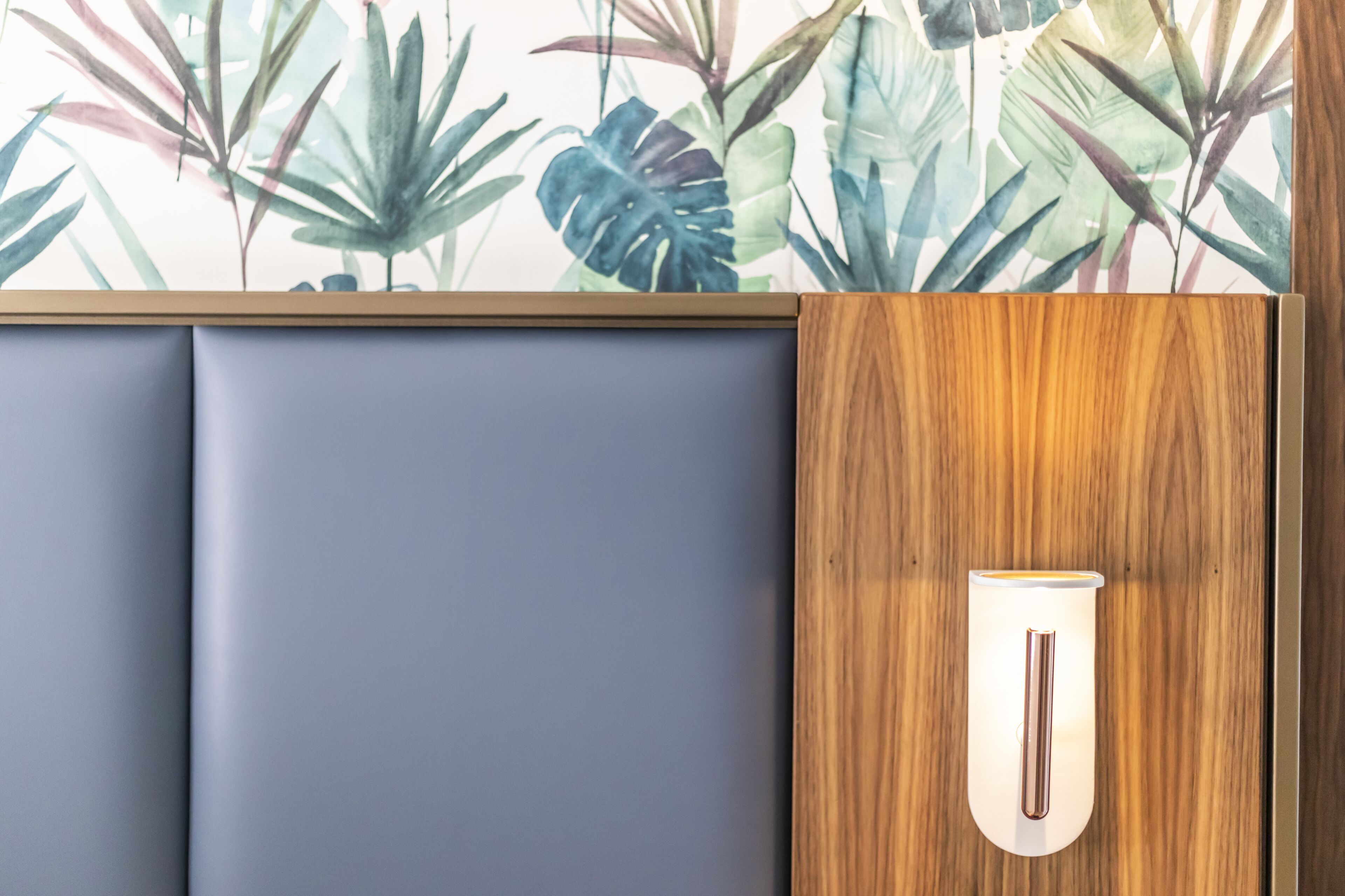 A room with a wooden panel wall, a grey cushioned seating area, and a wall-mounted light fixture.