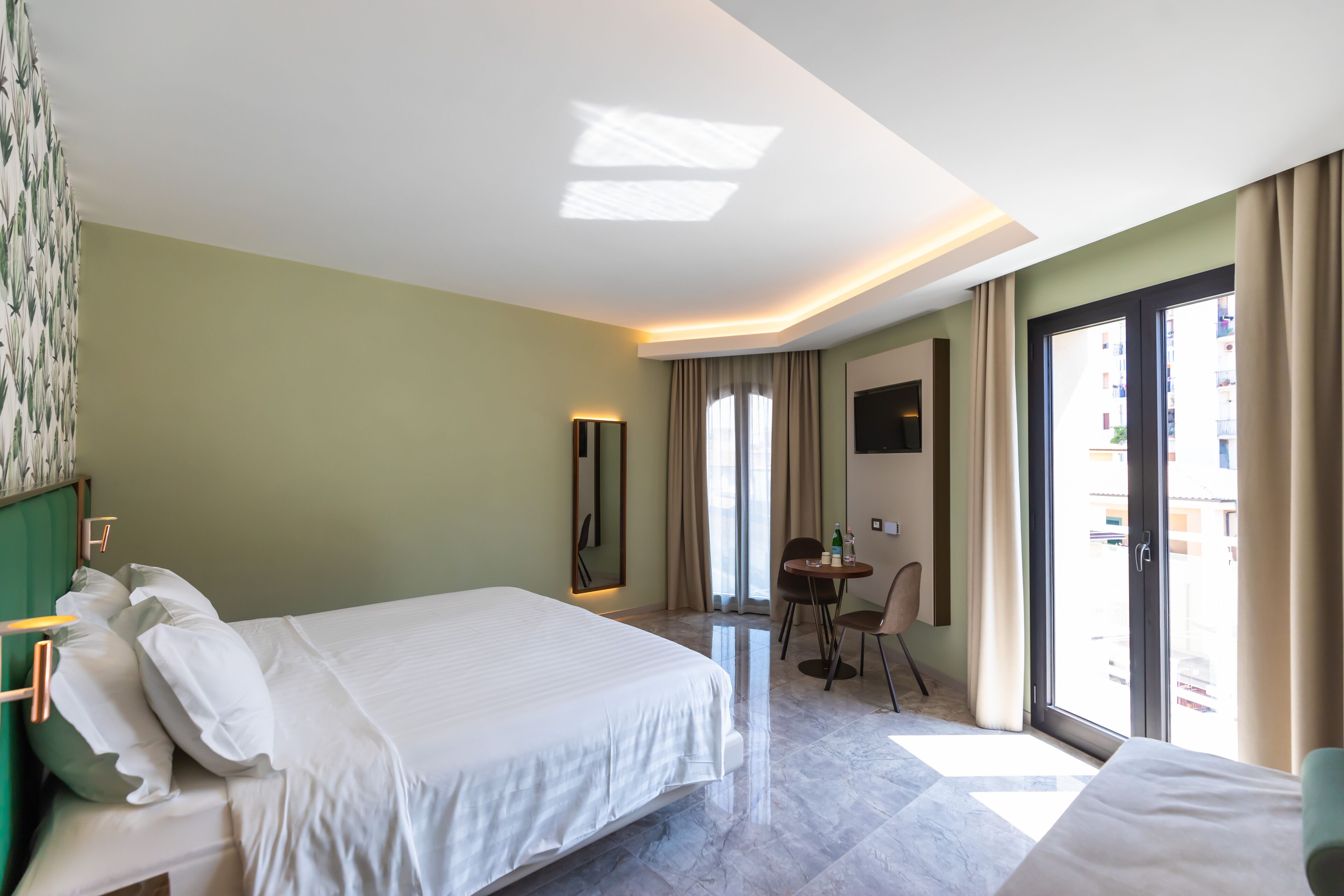 Habitación de hotel con una cama grande, un escritorio, una silla y un balcón con cortinas.
