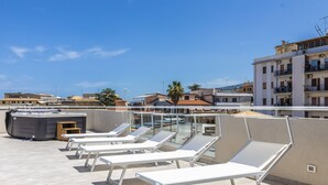 A rooftop terrace with sun loungers, a hot tub, and a view of the cityscape. - Solmaris Tropea - Rooms & Suites (Tropea)