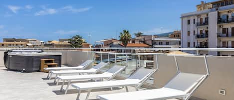 Una terraza en la azotea con tumbonas, un jacuzzi y vistas a la ciudad.