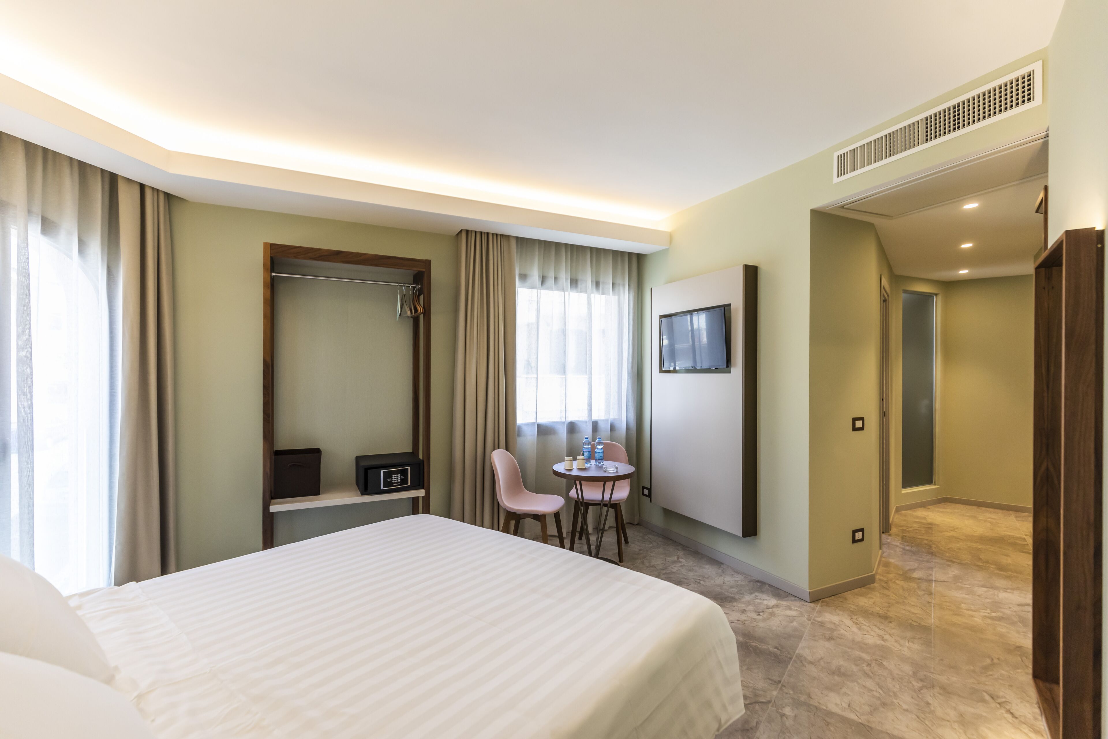 A hotel room with a large bed, a desk with a chair, a TV, and a wardrobe.