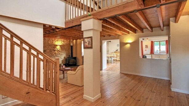 A spacious loft with exposed wooden beams, a stone wall, and a cozy seating area. - Tranquil and spacious gîte with own pool near market town (Lezay)