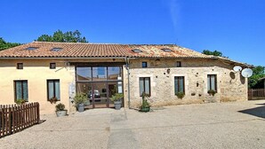 A two-story building with a tiled roof, a central entrance with glass doors, and potted plants in front. - Tranquil and spacious gîte with own pool near market town (Lezay)
