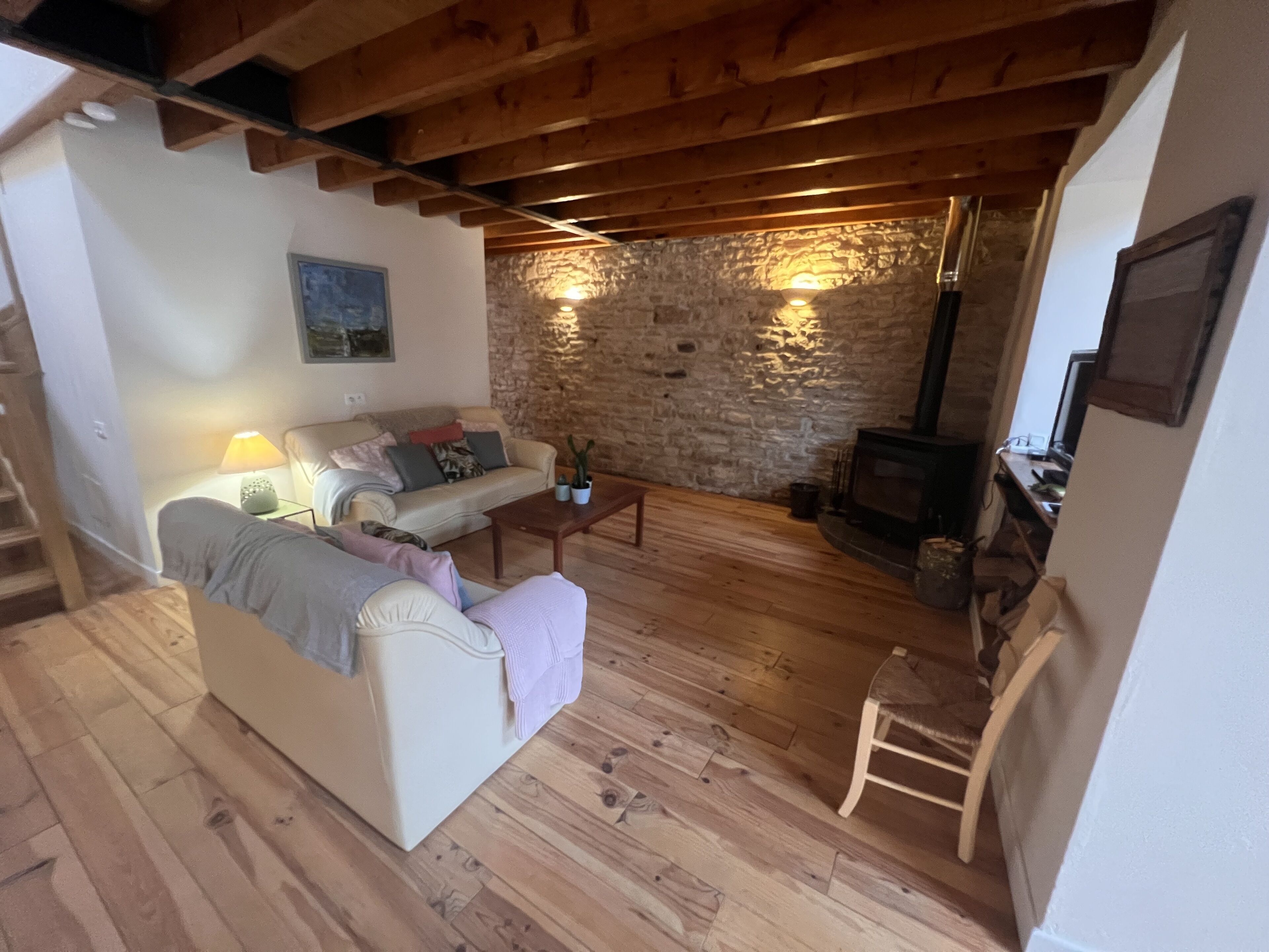 A cozy living room with a stone wall, wooden beams, a fireplace, and a sofa.