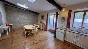 A cozy kitchen with wooden flooring, a dining table with chairs, a stone wall, and a skylight. - Tranquil and spacious gîte with own pool near market town (Lezay)