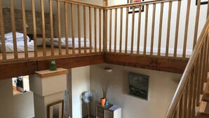 A loft bedroom with a wooden ceiling, a bed, a small table with a vase, and a fan. - Tranquil and spacious gîte with own pool near market town (Lezay)