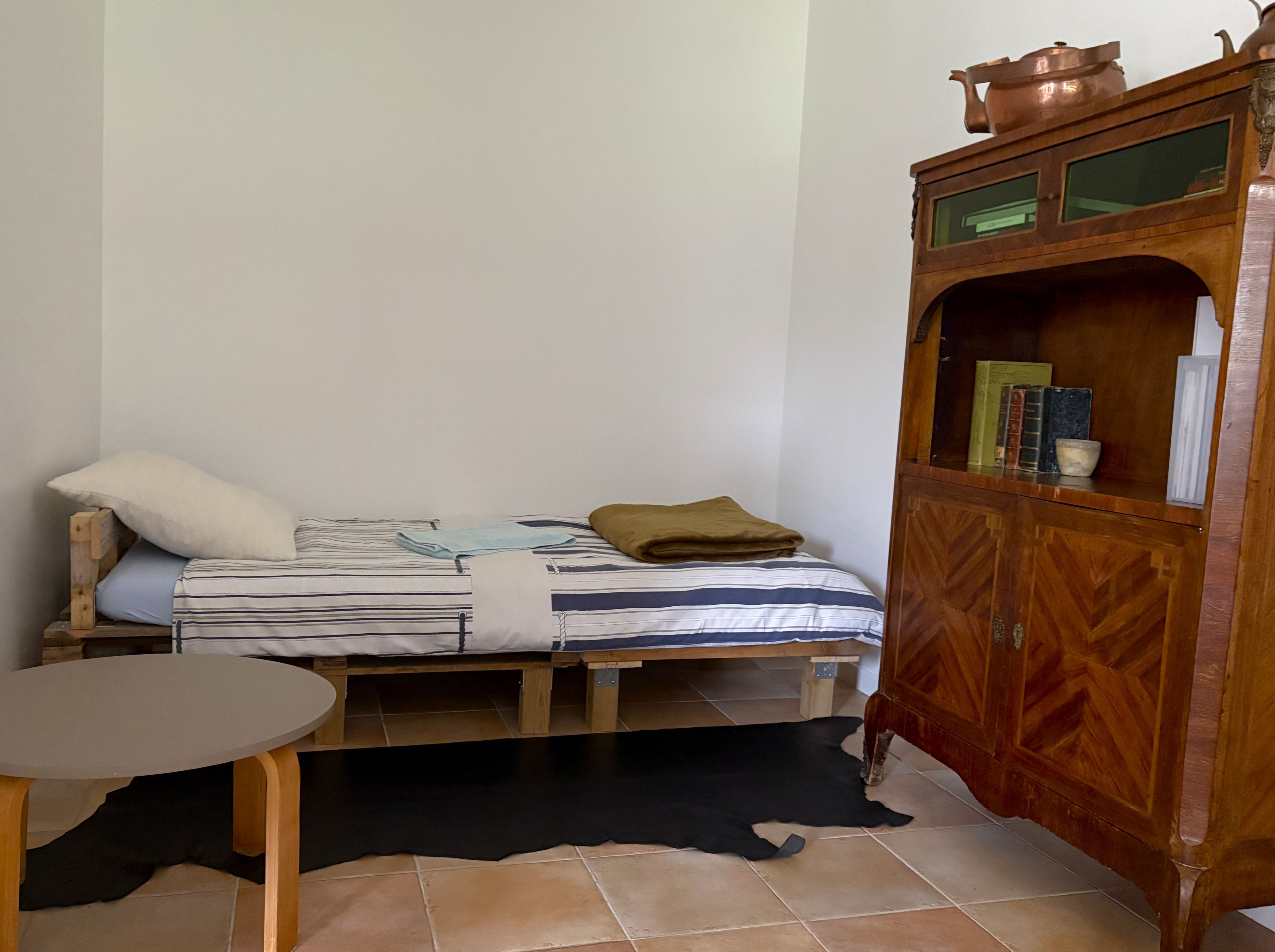 Une petite pièce, de taille modeste, comprenant un lit, une armoire en bois et une petite table.