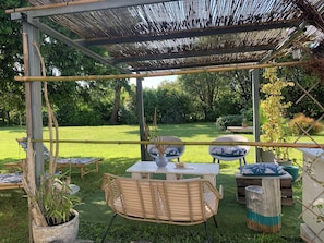An outdoor seating area with bamboo furniture, a pergola, and a view of a lush garden.