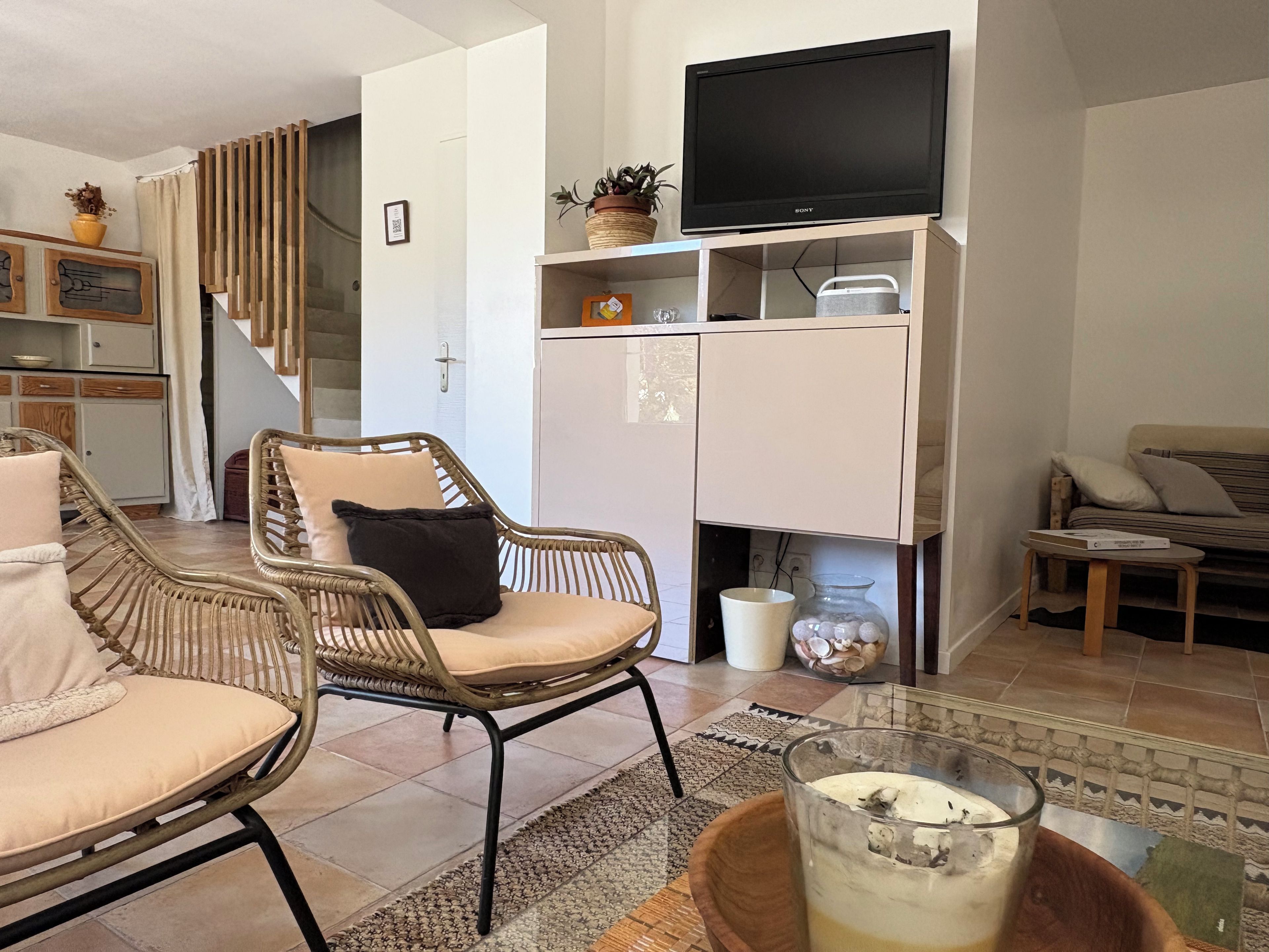 Een woonkamer met rieten stoelen, een bank, een flatscreen televisie en een keuken in de achtergrond.