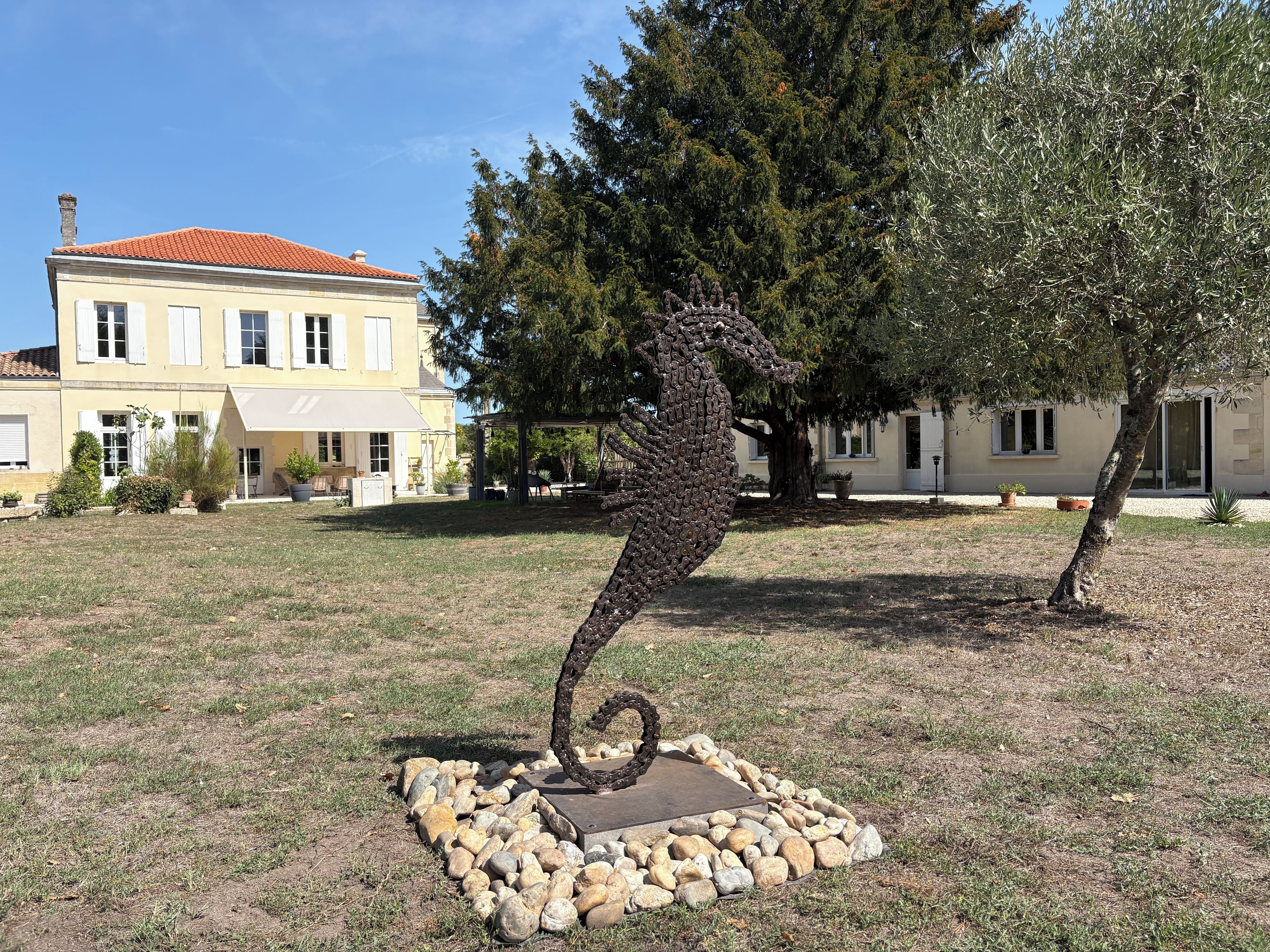 Une sculpture représentant un hippocampe dans un jardin, avec une maison en arrière-plan.