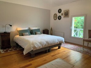 Quarto com cama, piso de madeira, mesa de cabeceira, luminária, janela e cadeira.