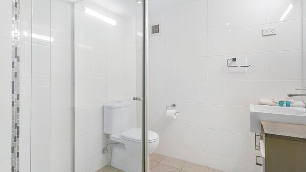 Ein modernes Badezimmer mit Duschkabine aus Glas, Toilette und Waschbeckenbereich mit Handtuch und Pflegeprodukten.