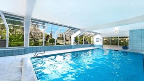 En indendørs swimmingpool med glasvægge, flisegulv og en badestige.