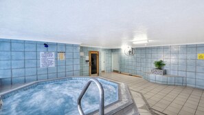 Ett spaområde med ett bubbelbad, kaklade väggar, en dörr och en väggmonterad fläkt.