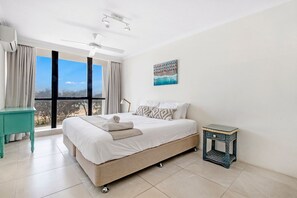 A bedroom with a large bed, a small table, a painting, and a view of the outdoors.