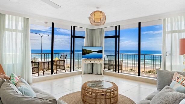 A spacious living room with a large TV, wicker furniture, and a view of the beach.