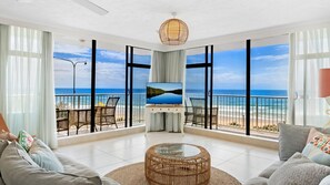 Ein geräumiges Wohnzimmer mit großem Fernseher, Korbmöbeln und Blick auf den Strand.