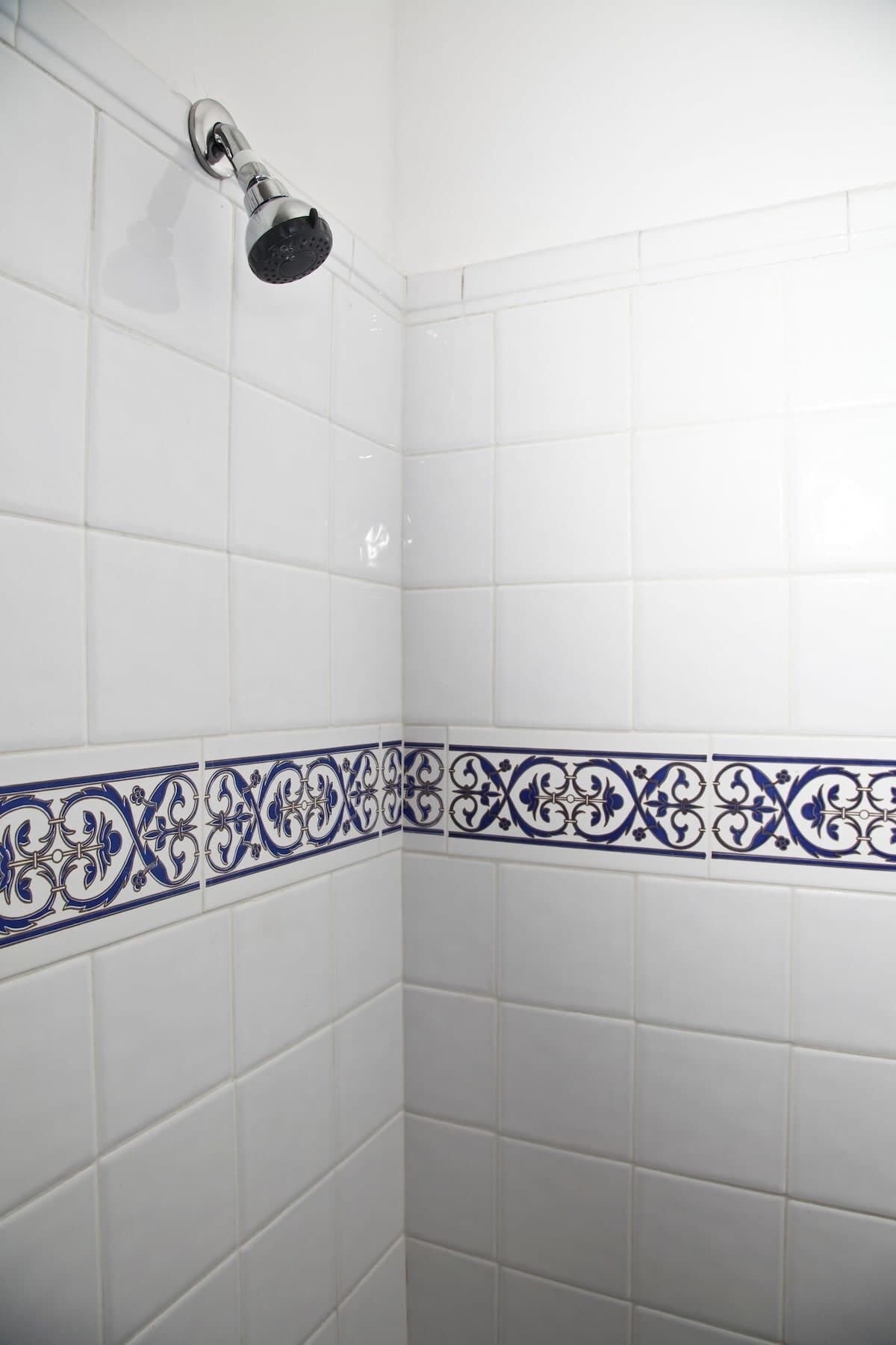 Esquina de un baño con azulejos blancos y un borde decorativo azul.