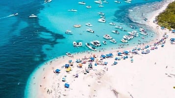 Vista aérea de una playa con numerosas embarcaciones fonqueadas en el agua y gente en la orilla.