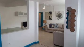 Un salon moderne avec un canapé, une table basse et une lampe. Il y a également un coin cuisine avec des placards et un plan de travail.