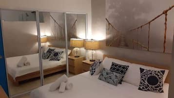 Een slaapkamer met een bed, nachtkastjes, lampen, een spiegel en een kunstwerk aan de muur.