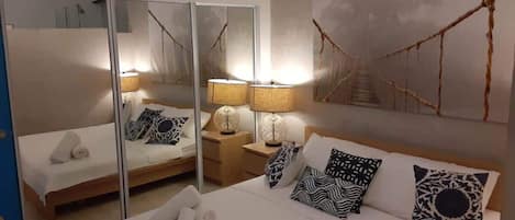 A bedroom with a bed, bedside tables, lamps, a mirror, and a wall art piece.