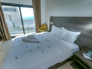 A hotel room with a large bed, a wooden headboard, a yellow armchair, and a view of the sea through large windows. - Hotel Marina Dreams Dakhla (Dakhla)